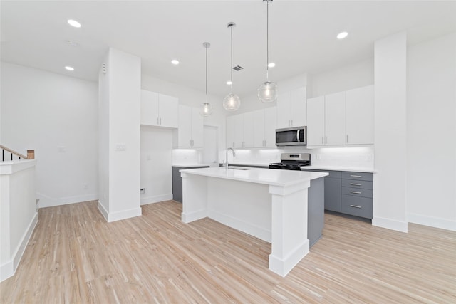 2103 Holman, Houston, TX 77004 - kitchen with appliances with stainless steel finishes, light wood-type flooring, a center island with sink, white cabinets, and recessed lighting