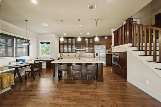 959 W 42nd St, Houston, TX 77018 - kitchen featuring built in appliances, light countertops, dark brown cabinetry, glass insert cabinets, and a kitchen bar