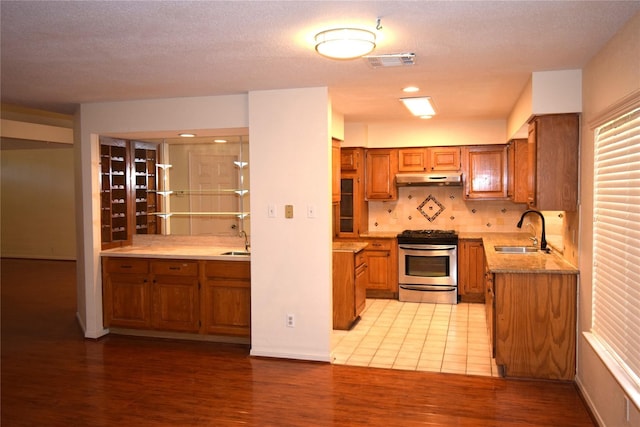2926 Field Line Dr, Sugar Land, TX 77479 - kitchen featuring stainless steel gas range, brown cabinetry, under cabinet range hood, light wood-style flooring, and decorative backsplash