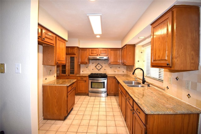 2926 Field Line Dr, Sugar Land, TX 77479 - kitchen with gas stove, under cabinet range hood, brown cabinets, light stone counters, and decorative backsplash