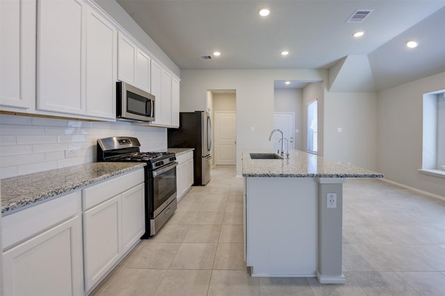 32014 Quail Terrace Ln, Conroe, TX 77385 - kitchen featuring appliances with stainless steel finishes, decorative backsplash, white cabinets, a center island with sink, and light stone countertops