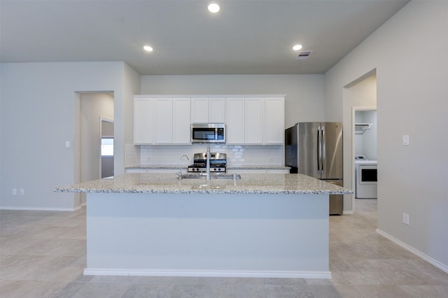 32014 Quail Terrace Ln, Conroe, TX 77385 - kitchen featuring appliances with stainless steel finishes, washer / dryer, a center island with sink, decorative backsplash, and light stone counters