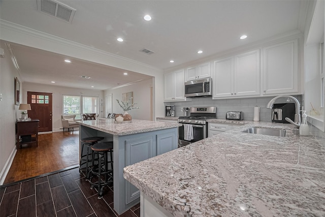 1931 Ansbury Dr, Houston, TX 77018 - kitchen with appliances with stainless steel finishes, a kitchen island, white cabinetry, crown molding, and backsplash