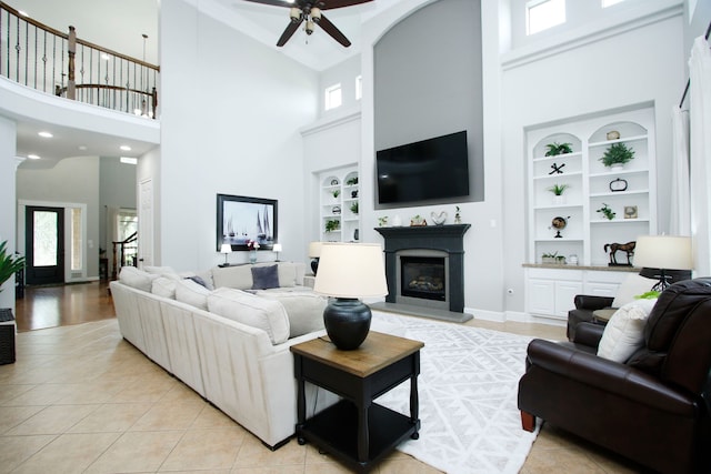 9303 Georgetown Glen Cir, Cypress, TX 77433 - living area with a high ceiling, built in features, a glass covered fireplace, ceiling fan, and light tile patterned floors