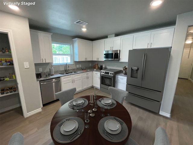 7916 Tate St, Houston, TX 77028 - kitchen featuring appliances with stainless steel finishes, white cabinets, light wood-style flooring, light stone counters, and recessed lighting