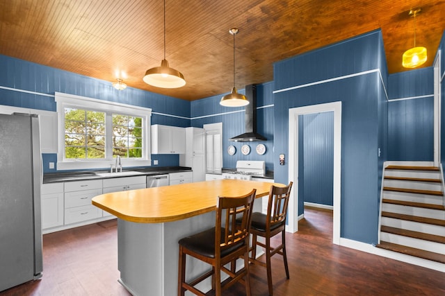 1002 E Gonzales St, Yoakum, TX 77995 - kitchen featuring wall chimney exhaust hood, appliances with stainless steel finishes, dark wood-style floors, white cabinets, and a kitchen breakfast bar