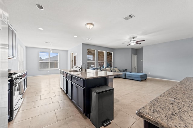 4330 Barchetta Trl, Katy, TX 77493 - kitchen with stainless steel range with gas cooktop, a ceiling fan, light tile patterned flooring, light stone countertops, and an island with sink