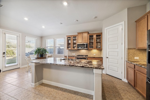 714 Fresh Sage Xing, Richmond, TX 77406 - kitchen featuring stainless steel microwave, dark stone countertops, a center island with sink, decorative backsplash, and light tile patterned floors