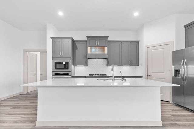 6226 Pelican Ridge Way, League City, TX 77573 - kitchen with appliances with stainless steel finishes, gray cabinetry, an island with sink, light countertops, and light wood finished floors
