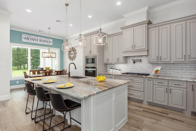 27647 N Salado Ct, Splendora, TX 77372 - kitchen with appliances with stainless steel finishes, tasteful backsplash, light wood finished floors, a kitchen island with sink, and crown molding