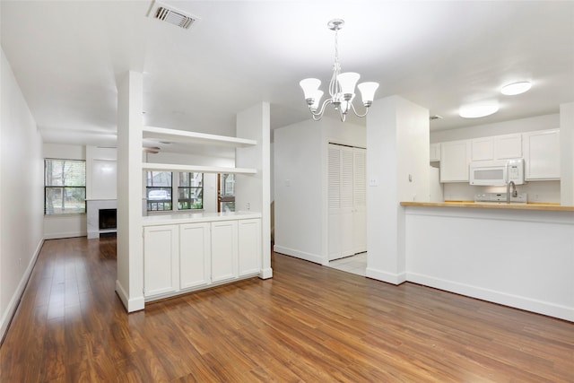 28 Sawmill Grove Ln, The Woodlands, TX 77380 - kitchen featuring white microwave, wood finished floors, a chandelier, a fireplace, and light countertops