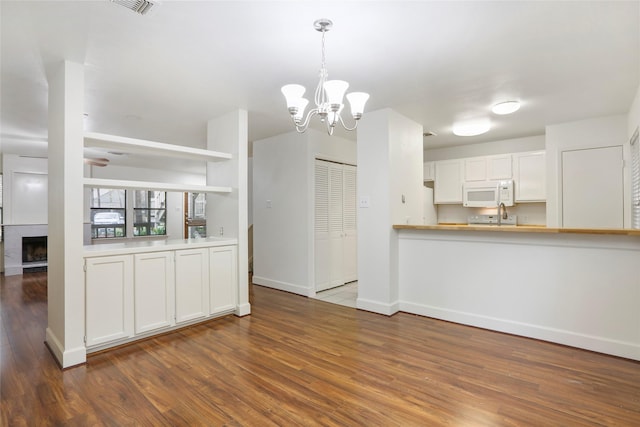 28 Sawmill Grove Ln, The Woodlands, TX 77380 - kitchen with white microwave, wood finished floors, a chandelier, white cabinetry, and a large fireplace