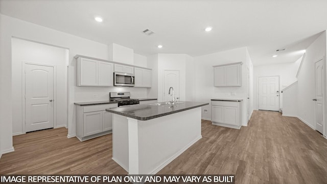5434 Magnolia Heath Ln, Spring, TX 77373 - kitchen with stainless steel microwave, gas range, light wood finished floors, dark countertops, and an island with sink