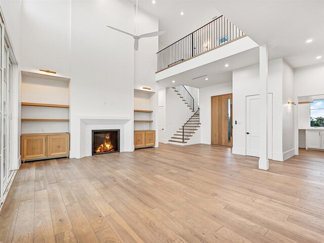 430 81st St, Galveston, TX 77554 - unfurnished living room featuring a high ceiling, light wood-style flooring, stairs, a glass covered fireplace, and built in shelves