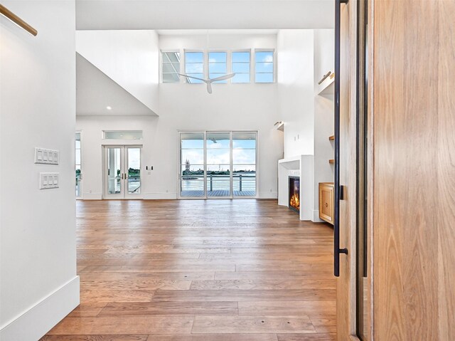 430 81st St, Galveston, TX 77554 - unfurnished living room with light wood-type flooring, a high ceiling, and a warm lit fireplace