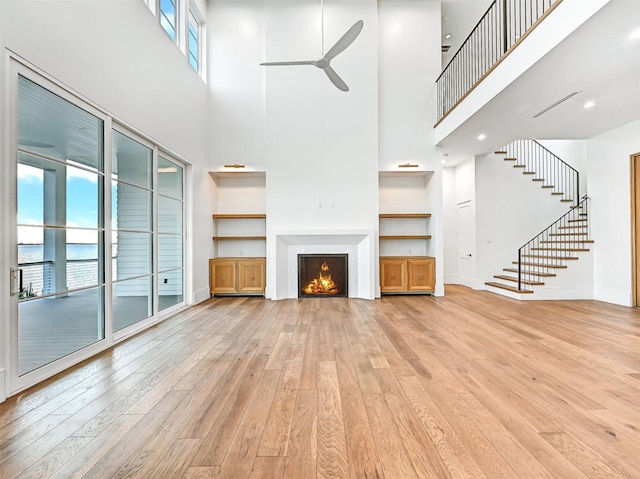 430 81st St, Galveston, TX 77554 - unfurnished living room featuring a towering ceiling, light wood-type flooring, ceiling fan, plenty of natural light, and a warm lit fireplace