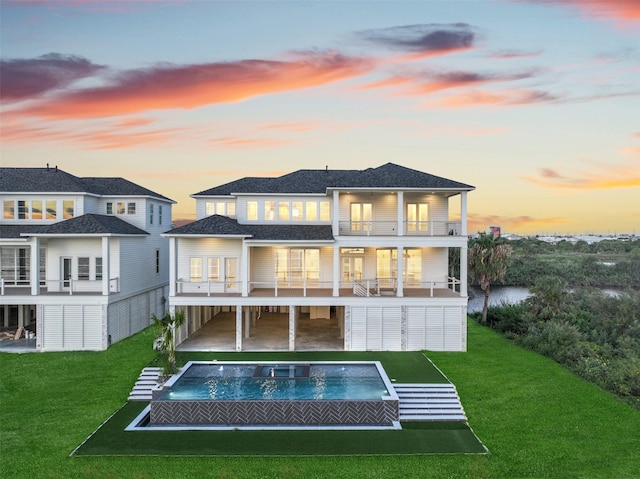 430 81st St, Galveston, TX 77554 - back of property at dusk featuring a balcony, an outdoor hot tub, an outdoor pool, a lawn, and a patio
