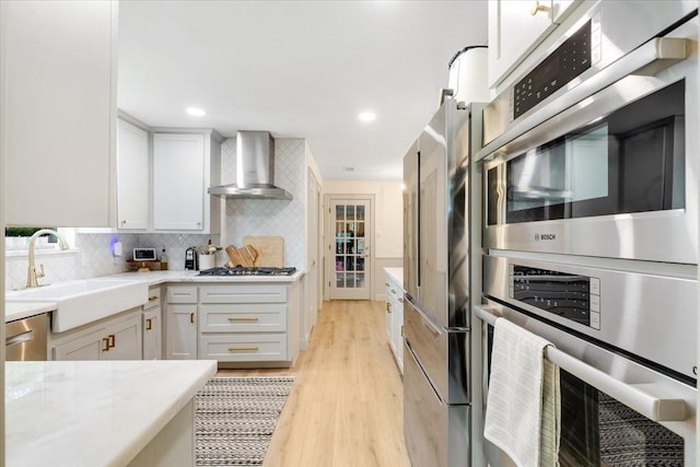 3220 Patricia Ln, Pearland, TX 77581 - kitchen with wall chimney range hood, appliances with stainless steel finishes, light wood-style floors, decorative backsplash, and white cabinetry