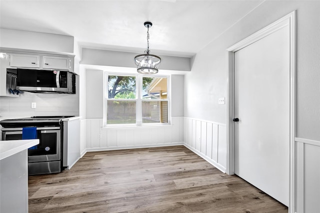 28207 Nancy Ln, Conroe, TX 77385 - kitchen with stainless steel appliances, wainscoting, a chandelier, hanging light fixtures, and light wood-style flooring