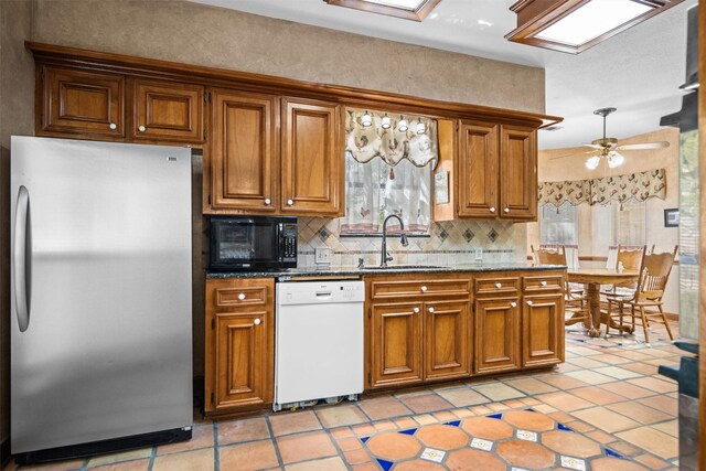215 Enchanted Estates Dr, Crockett, TX 75835 - kitchen featuring freestanding refrigerator, white dishwasher, black microwave, tasteful backsplash, and brown cabinetry