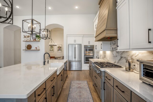 2603 Merlin Way, Katy, TX 77493 - kitchen with appliances with stainless steel finishes, a chandelier, arched walkways, premium range hood, and light wood-type flooring