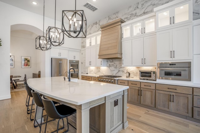 2603 Merlin Way, Katy, TX 77493 - kitchen featuring appliances with stainless steel finishes, custom range hood, a chandelier, an island with sink, and arched walkways