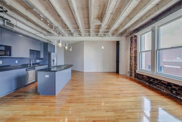 201 Main St Unit 5D, Houston, TX 77002 - kitchen with appliances with stainless steel finishes, dark countertops, brick wall, light wood-style flooring, and a kitchen island