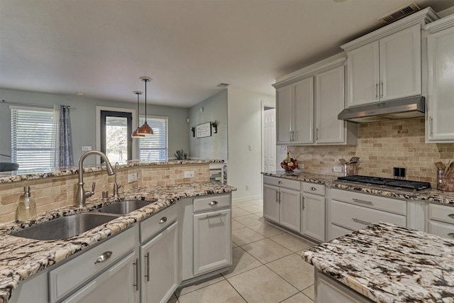 20210 Mariposa Blue Ln, Cypress, TX 77433 - kitchen with under cabinet range hood, stainless steel gas stovetop, decorative backsplash, light tile patterned floors, and light stone countertops