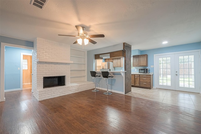 2307 N Thompson, Conroe, TX 77303 - unfurnished living room featuring a ceiling fan, french doors, light wood-style flooring, a brick fireplace, and built in shelves