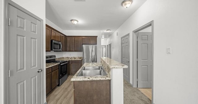235 Calloway St, Houston, TX 77029 - kitchen featuring stainless steel appliances, an island with sink, dark brown cabinets, light wood-style floors, and light stone counters
