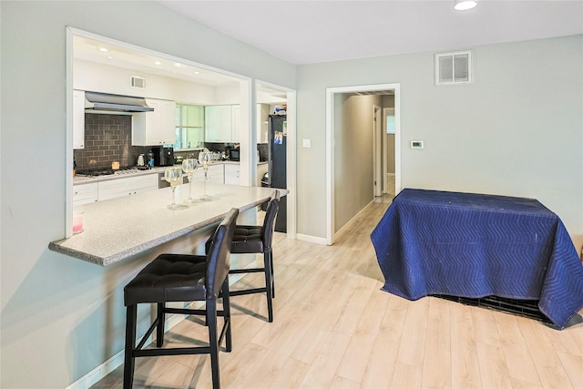 2706 Meadow Ln, La Marque, TX 77568 - kitchen with stainless steel gas stovetop, white cabinetry, a breakfast bar, exhaust hood, and light wood-type flooring