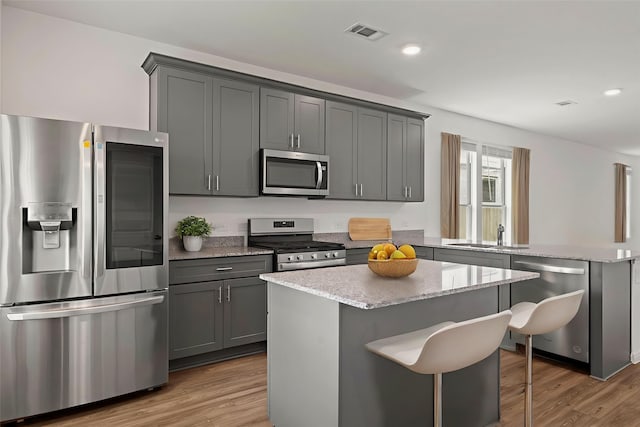 21127 Dolphin Bay Ln, Cypress, TX 77433 - kitchen featuring appliances with stainless steel finishes, wood finished floors, gray cabinets, light stone countertops, and a center island