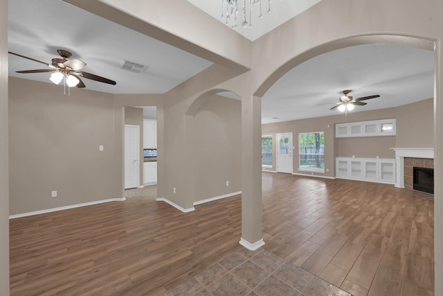 107 W Russet Grove Cir, The Woodlands, TX 77384 - unfurnished living room with a ceiling fan, wood finished floors, arched walkways, and a tiled fireplace