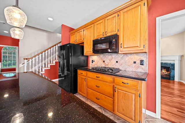 1808 Brookside Dr, Friendswood, TX 77546 - kitchen with black appliances, decorative backsplash, dark stone counters, a lit fireplace, and pendant lighting