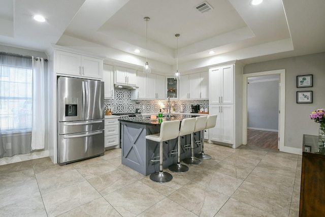 910 11th St, South Houston, TX 77587 - kitchen with stainless steel fridge, a tray ceiling, decorative backsplash, white cabinetry, and a breakfast bar