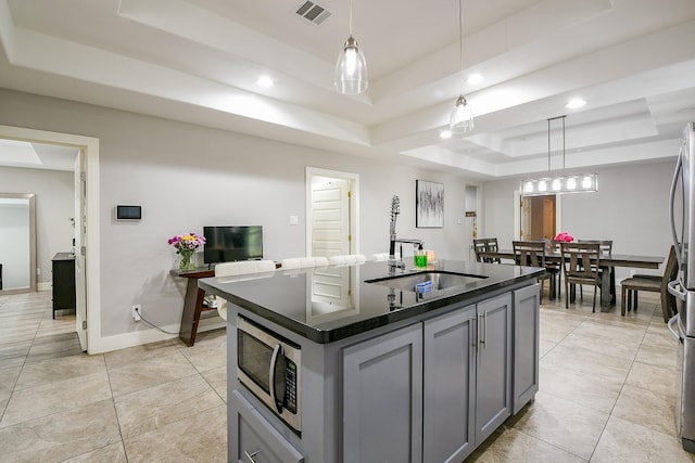 910 11th St, South Houston, TX 77587 - kitchen with a raised ceiling, stainless steel microwave, dark countertops, gray cabinets, and a center island with sink