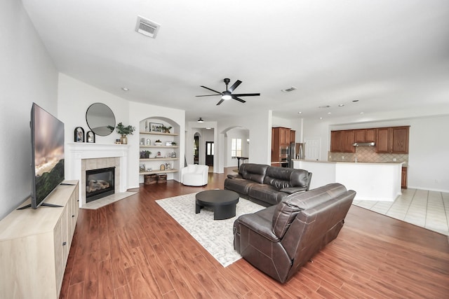 3214 Oak Park Ln, Missouri City, TX 77459 - living room featuring arched walkways, built in features, a tiled fireplace, a ceiling fan, and light wood-style floors