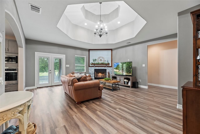 1415 Pony Ln, Simonton, TX 77485 - living area featuring a raised ceiling, a chandelier, light wood-type flooring, a stone fireplace, and arched walkways