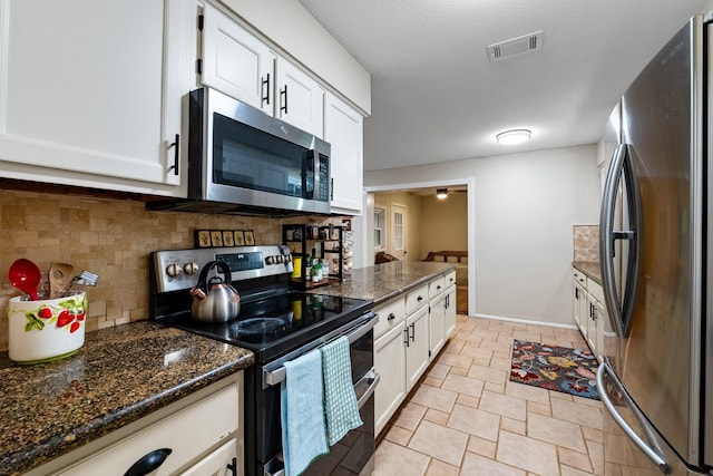 4205 Wade Rd, Brookshire, TX 77423 - kitchen featuring appliances with stainless steel finishes, backsplash, white cabinetry, light stone finish flooring, and dark stone counters