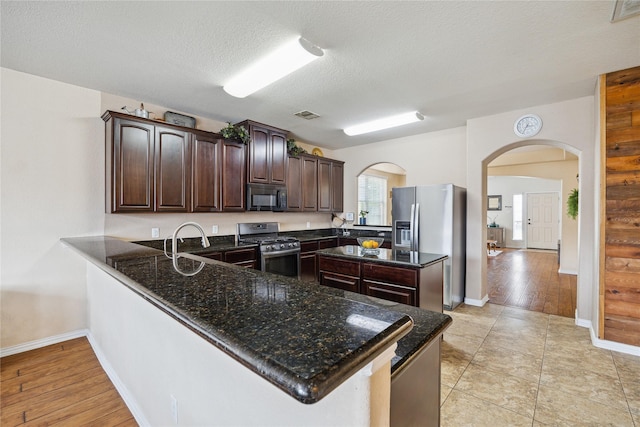 8234 Nagy Hill St, Spring, TX 77379 - kitchen with stainless steel appliances, arched walkways, dark brown cabinetry, a peninsula, and dark stone counters