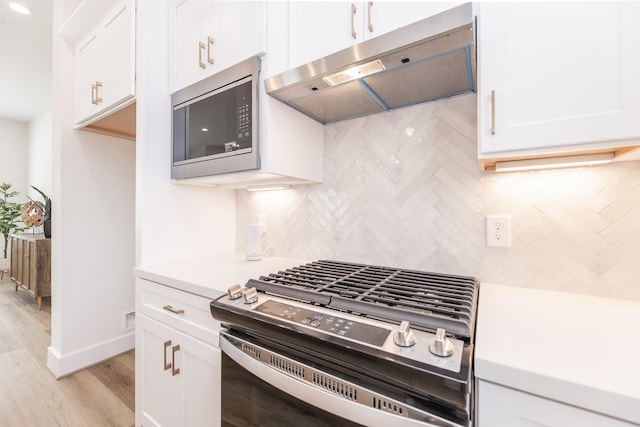 1615 Erin St, Houston, TX 77009 - kitchen featuring stainless steel appliances, under cabinet range hood, light countertops, decorative backsplash, and white cabinetry