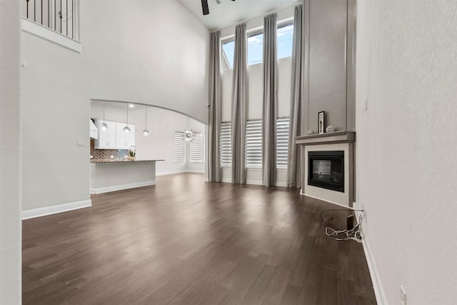 6126 Garden Lakes Ln, Sugar Land, TX 77479 - unfurnished living room featuring a ceiling fan, a glass covered fireplace, dark wood-style flooring, high vaulted ceiling, and arched walkways