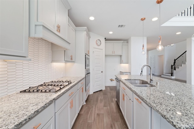 13731 Pedernales Ct, Cypress, TX 77429 - kitchen featuring appliances with stainless steel finishes, white cabinetry, hanging light fixtures, wood finished floors, and backsplash