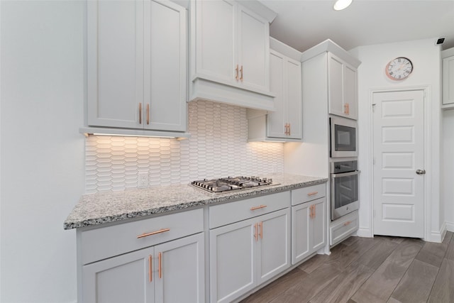 13731 Pedernales Ct, Cypress, TX 77429 - kitchen with appliances with stainless steel finishes, backsplash, light stone countertops, white cabinetry, and wood finished floors