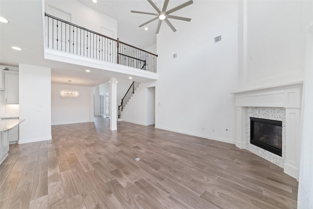 13731 Pedernales Ct, Cypress, TX 77429 - unfurnished living room featuring a fireplace, a ceiling fan, light wood-type flooring, a high ceiling, and a chandelier