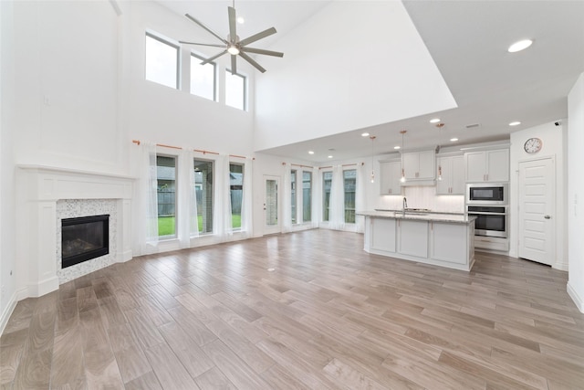 13731 Pedernales Ct, Cypress, TX 77429 - unfurnished living room featuring ceiling fan, a glass covered fireplace, a towering ceiling, light wood-type flooring, and recessed lighting