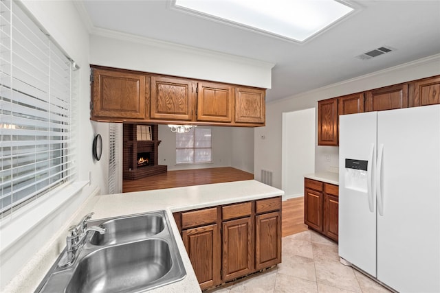 15207 Hillside Park Way, Cypress, TX 77433 - kitchen with white refrigerator with ice dispenser, ornamental molding, light countertops, a brick fireplace, and brown cabinets