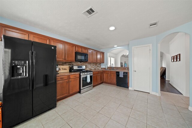 1111 Cypress Ln, Dayton, TX 77535 - kitchen featuring black appliances, arched walkways, brown cabinetry, backsplash, and light tile patterned floors