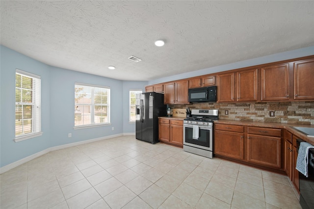 1111 Cypress Ln, Dayton, TX 77535 - kitchen featuring stainless steel range with gas cooktop, black microwave, refrigerator with ice dispenser, backsplash, and a textured ceiling