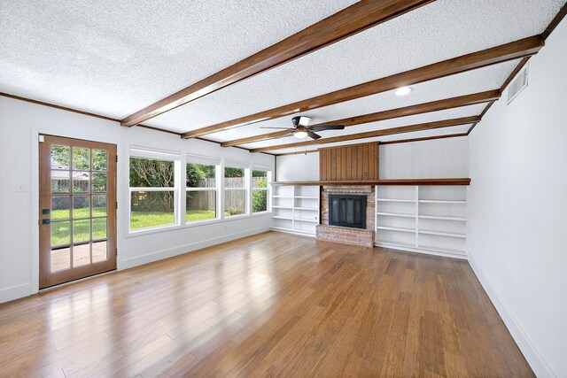 12239 Monticeto Ln, Meadows Place, TX 77477 - unfurnished living room featuring a textured ceiling, wood finished floors, a ceiling fan, beamed ceiling, and a fireplace